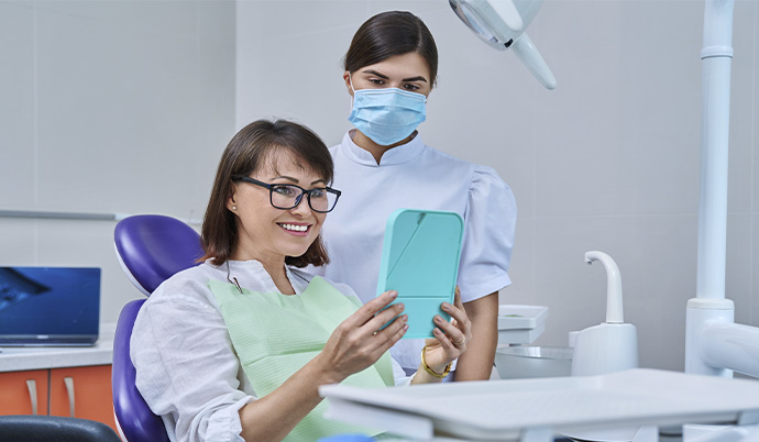 mulher sorrindo ao ver o resultado de seu implante no consultório de uma dentista