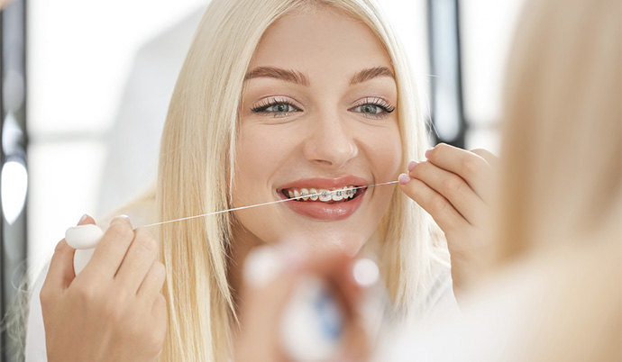 mulher que usa aparelho convencional passando fio dental em frente ao espelho