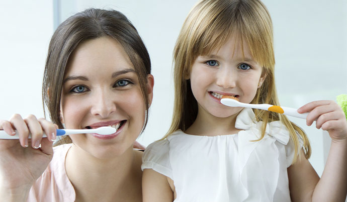 Mãe ensinando a filha como escovar os dentes.