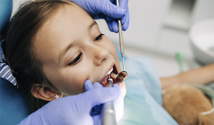 menina tendo seus dentes avaliados por um odontopediatra