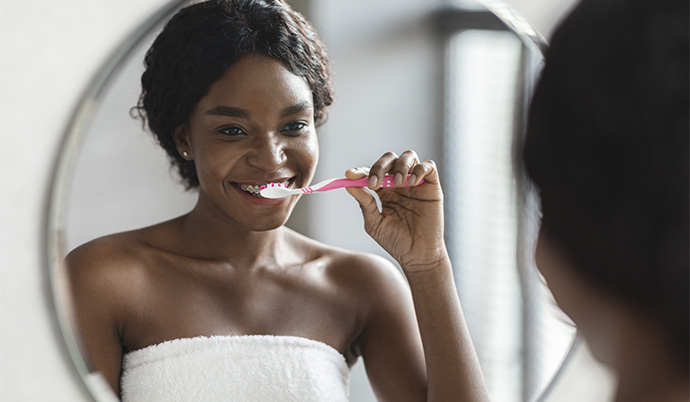 mulher que usa aparelho convencional escovando os dentes em frente ao espelho