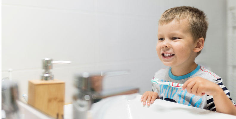 Criança escovando os dentes em frente ao espelho