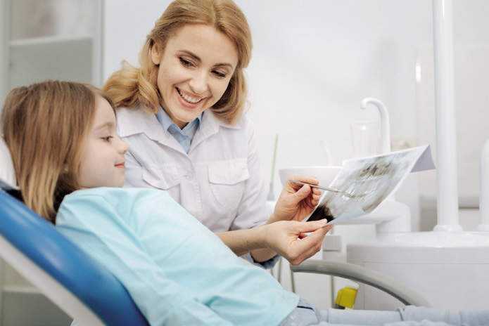 Dentista mostrando imagem de arcada dentária para criança que está sentada sorrindo